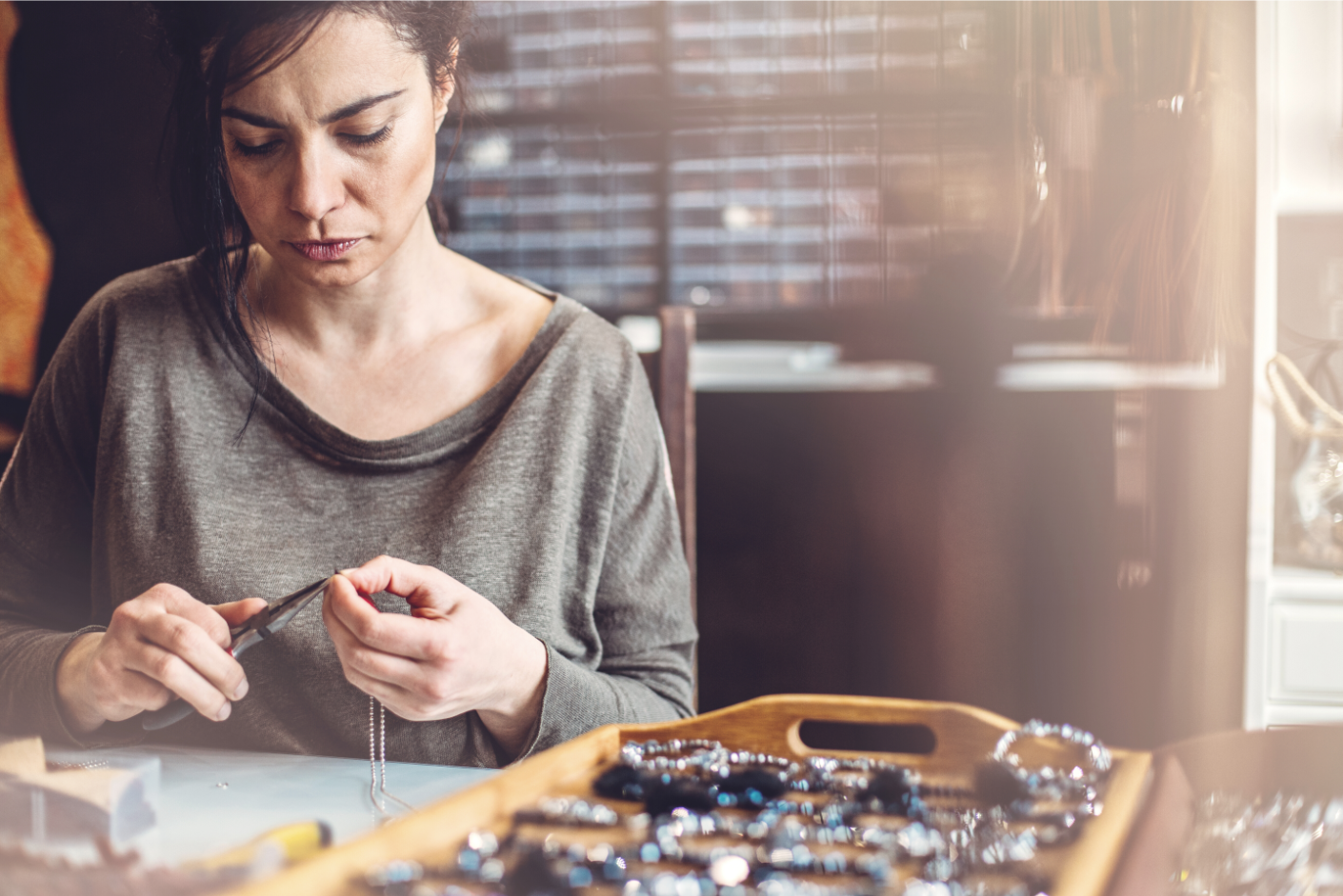 "Eine Frau fertigt mit Liebe ein handgefertigtes Perlenarmband aus natürlichen Heilsteinen für MANA'OLANA® – einzigartiger Schmuck für Harmonie und Balance."